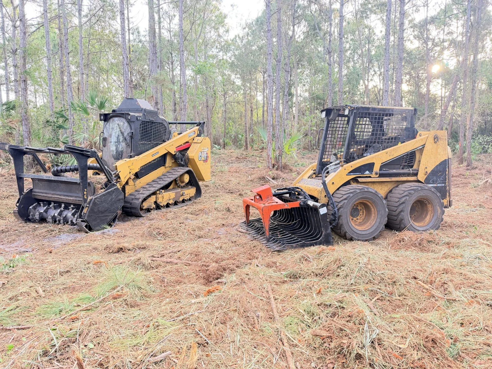 Mulcher and grapple skid steers side by side on cleared ground