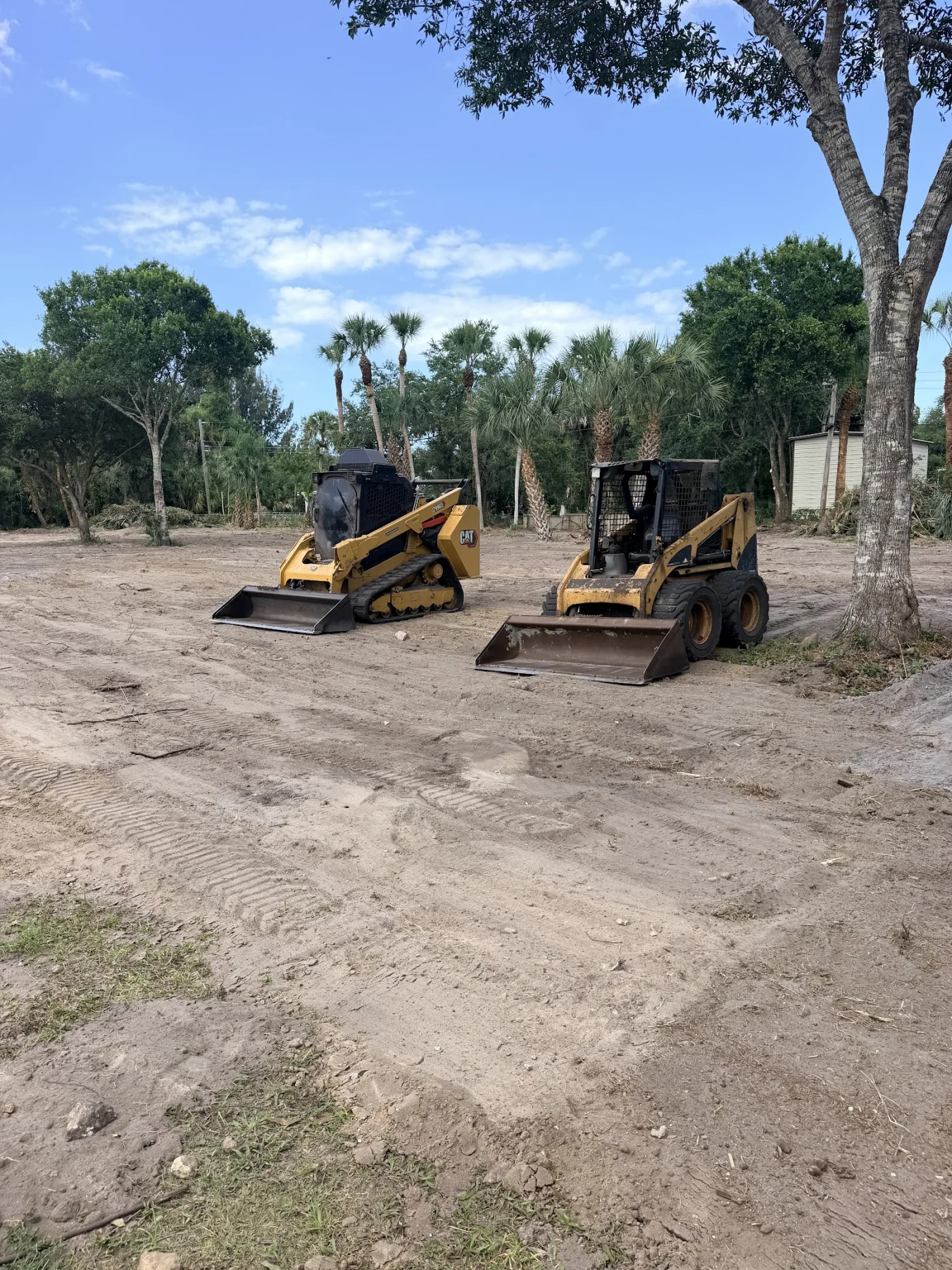 Two tracked skid steers staged on a prepared pad